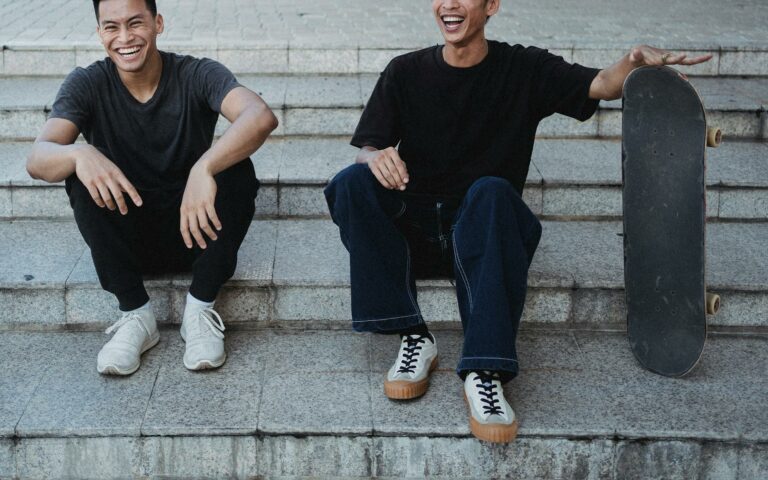 crop cheerful asian male friends resting on street steps